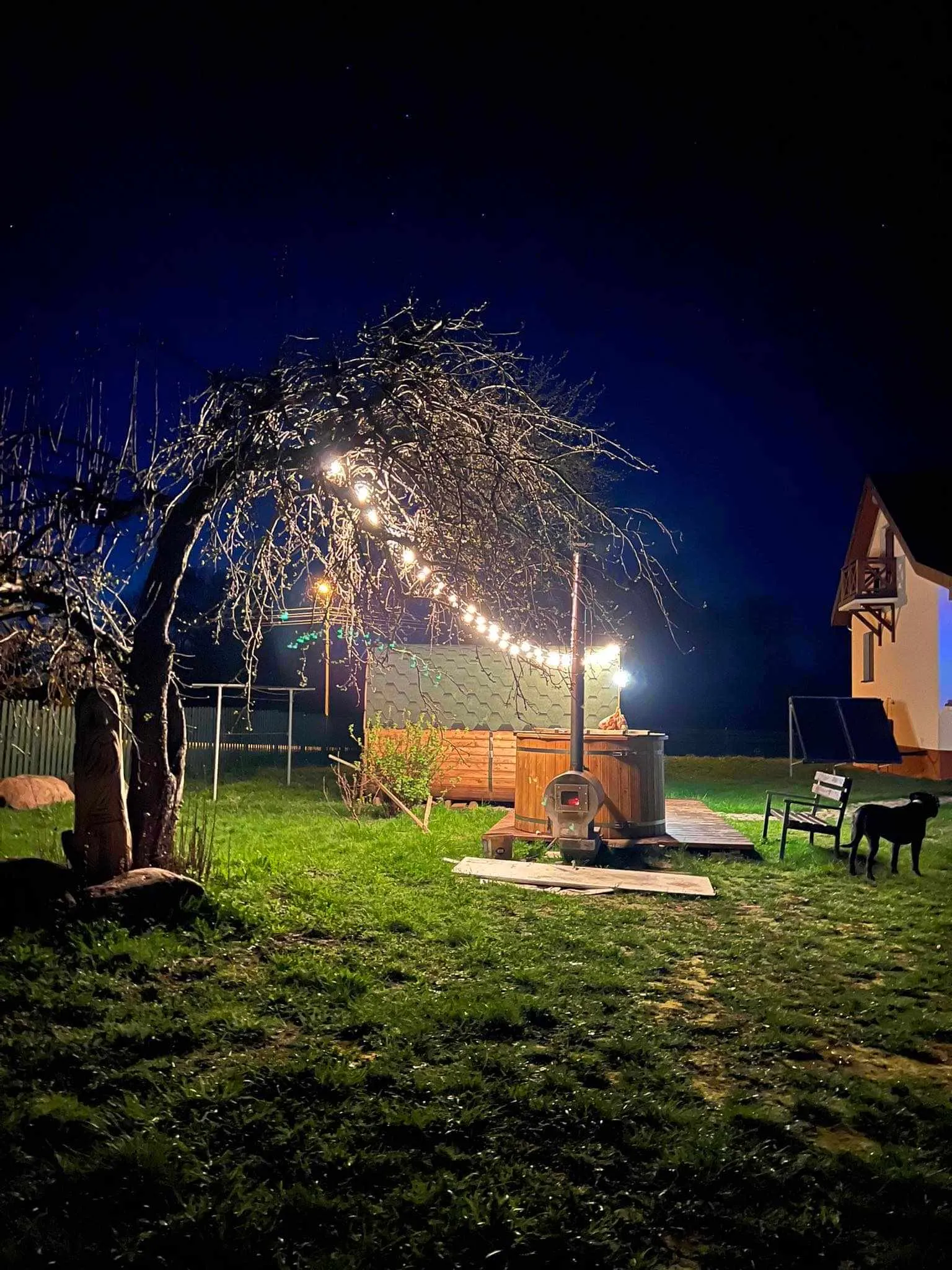 Bania i sauna w ogrodzie nocą, nad nimi girlanda świateł