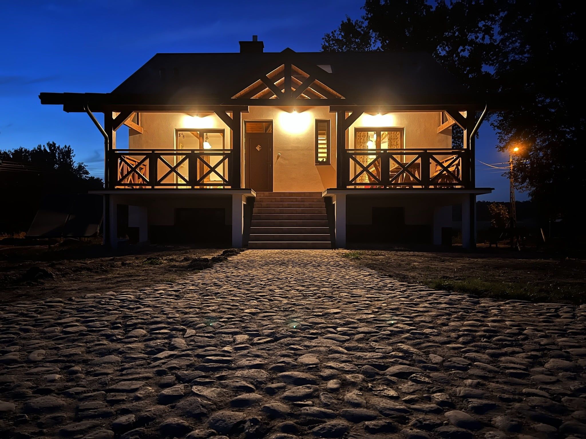 Kasztanówka nocą – podświetlona weranda drewnianego domu na Podlasiu